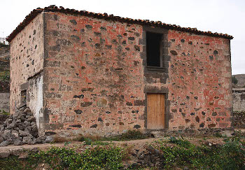 Vivienda de dos plantas con techumbre a cuatro aguas de planta rectangular. Empleo de sillares en las esquinas y vanos. En su eje central sobresale la puerta y ventana con repisa labrada. Encalado parcial dejando las piedras vistas y pintado de color rojo. Arucas, Gran Canaria.